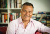 An author photograph of Stan Grant, pictured in front of a bookshelf