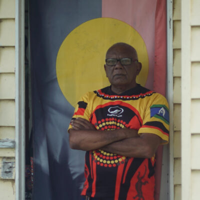 Lionel Fogarty standing in front of an Aboriginal flag.