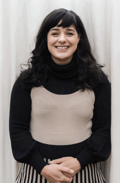 A photograph of Bryony McGuinness standing front of a curtain. She has black hair and is smiling.