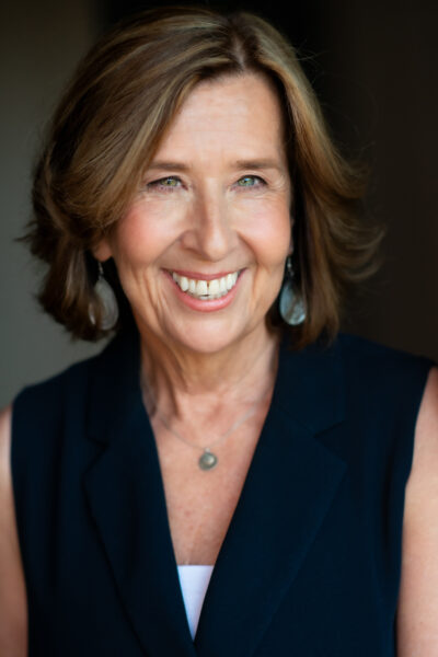 A portrait of Kathryn Heyman. She is wearing a black shirt and smiling.