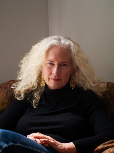 a portrait of Kirsty Murray. She has long curly blonde hair and is wearing a black top.