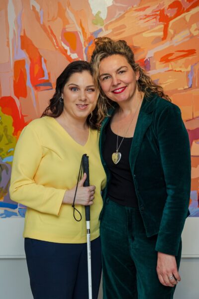 Nas Campanella and Eliza Hull in front of Richard Dunn's painting, Redbank Gorge, MacDonnell Ranges, c. 1936-37 (after Albert Namatjira), 2002-2010, from the Commonwealth Bank of Australia Collection. Copyright The Estate of Richard Dunn, courtesy Charles Nodrum Gallery. Photograph by Tim Harris, Red Antler Photography.