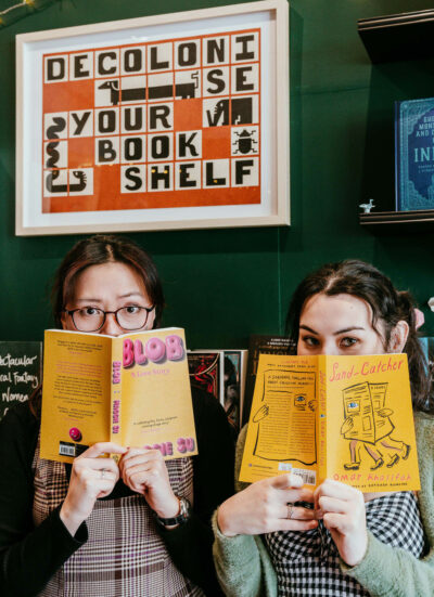 Marina and Xuan holding books over their mouths. A sign in the back reads 