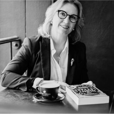 Photo of Jane Curry with book and coffee on desk.
