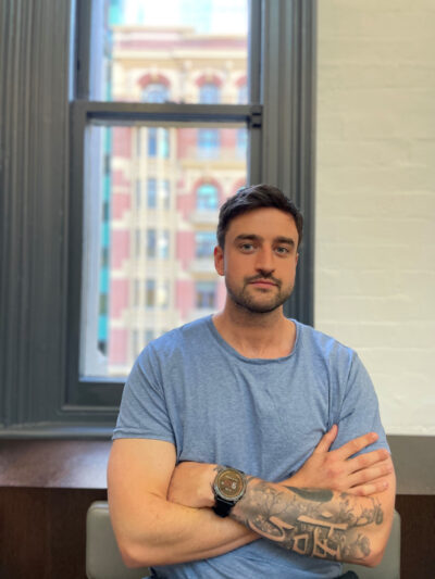 Photograph of Matt Rogers in front of a window, arms folded