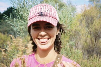 Photograph of Mia Thom in a hat in front of some green vegetation