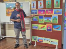 A person stands beside a series of images, gesturing at one of them, in a classroom environment